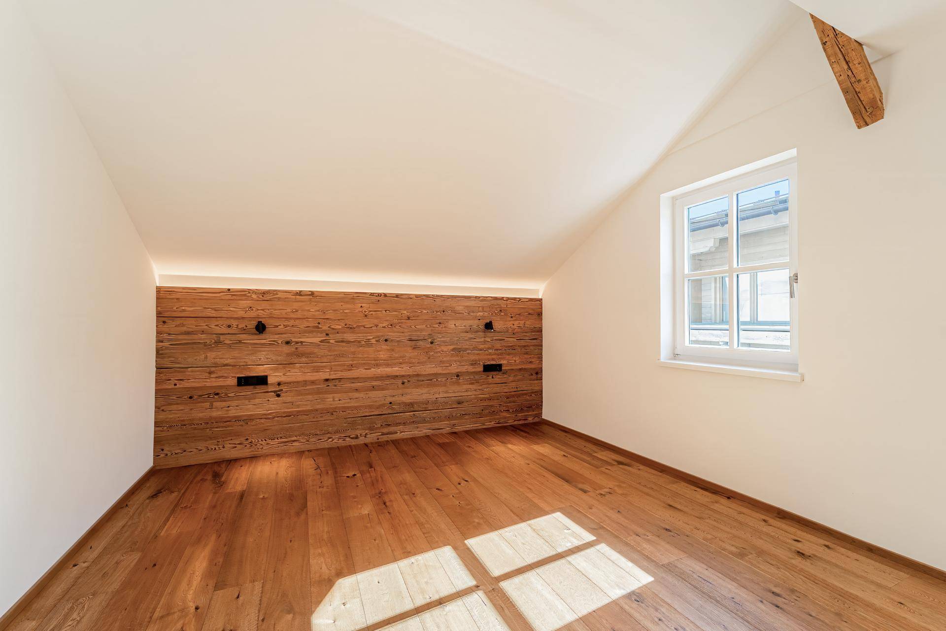 Gemütliches Schlafzimmer im Dachgeschoss mit Holzboden, Holzvertäfelung und viel Tageslicht.