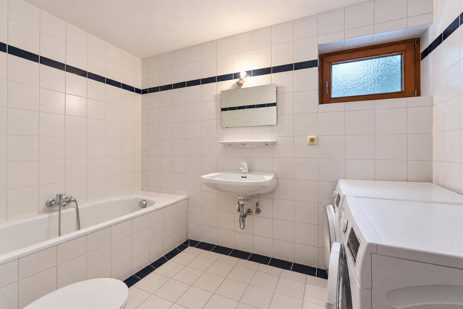 Funktionales Badezimmer mit Badewanne, Waschbecken, WC und Waschmaschine.