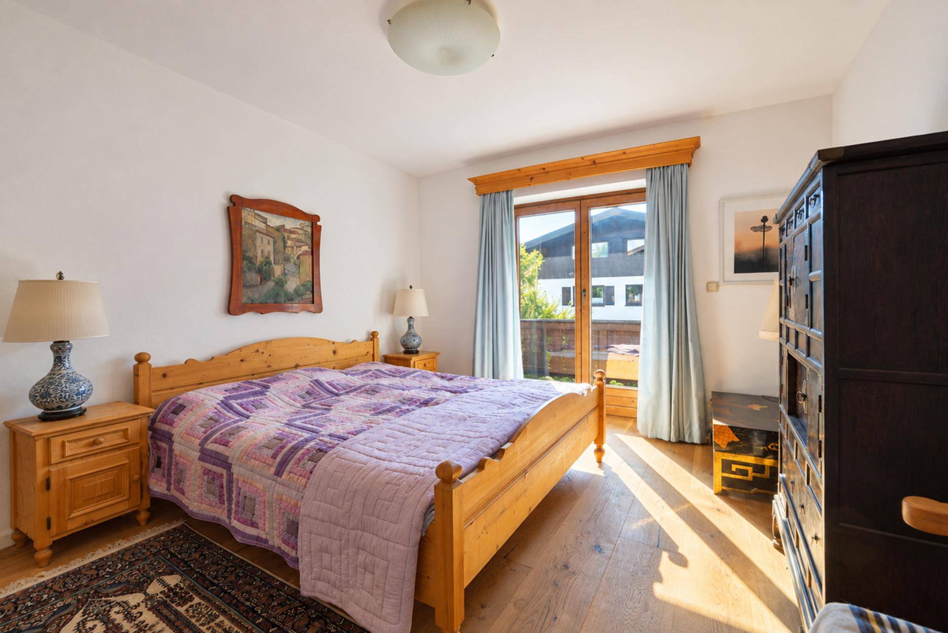 Gemütliches Schlafzimmer mit Holzbett, Nachttischen und Zugang zu einem Balkon.
