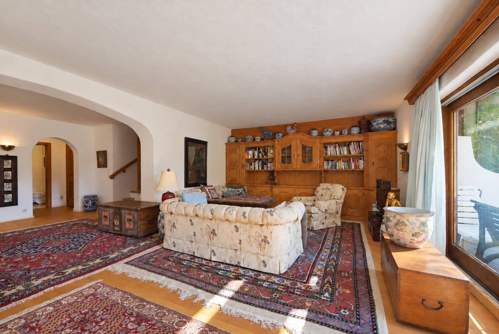 Geräumiges Wohnzimmer mit Holzboden, traditionellen Teppichen und großem Bücherregal.