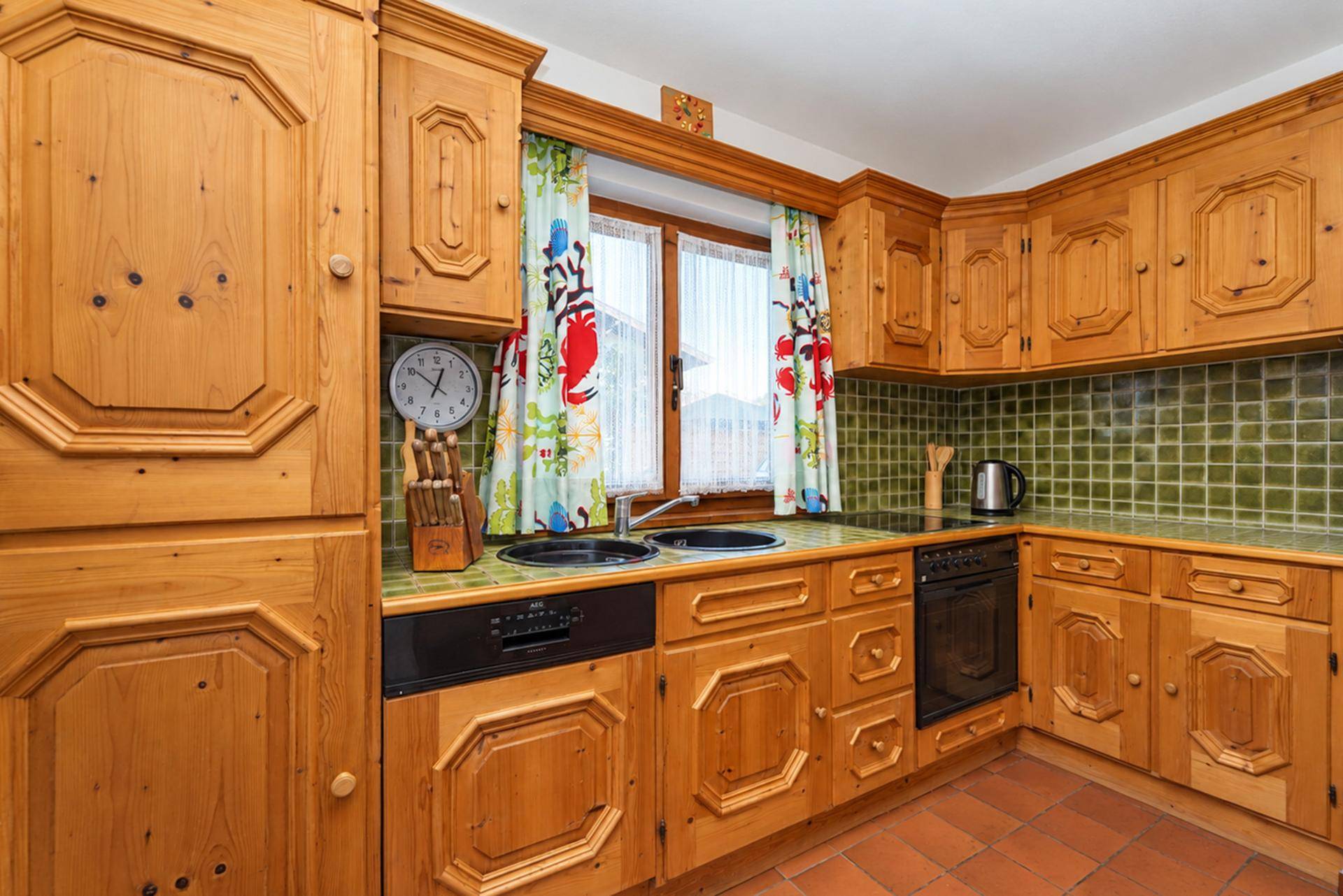 Rustikale Holzküche mit grünen Fliesen, Terrakottaboden und traditionellen Vorhängen.