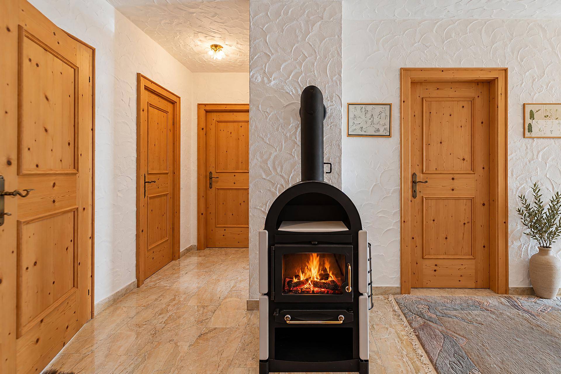 Heller Flur mit Fliesenboden, Holztüren und einem modernen Holzofen als Blickfang.
