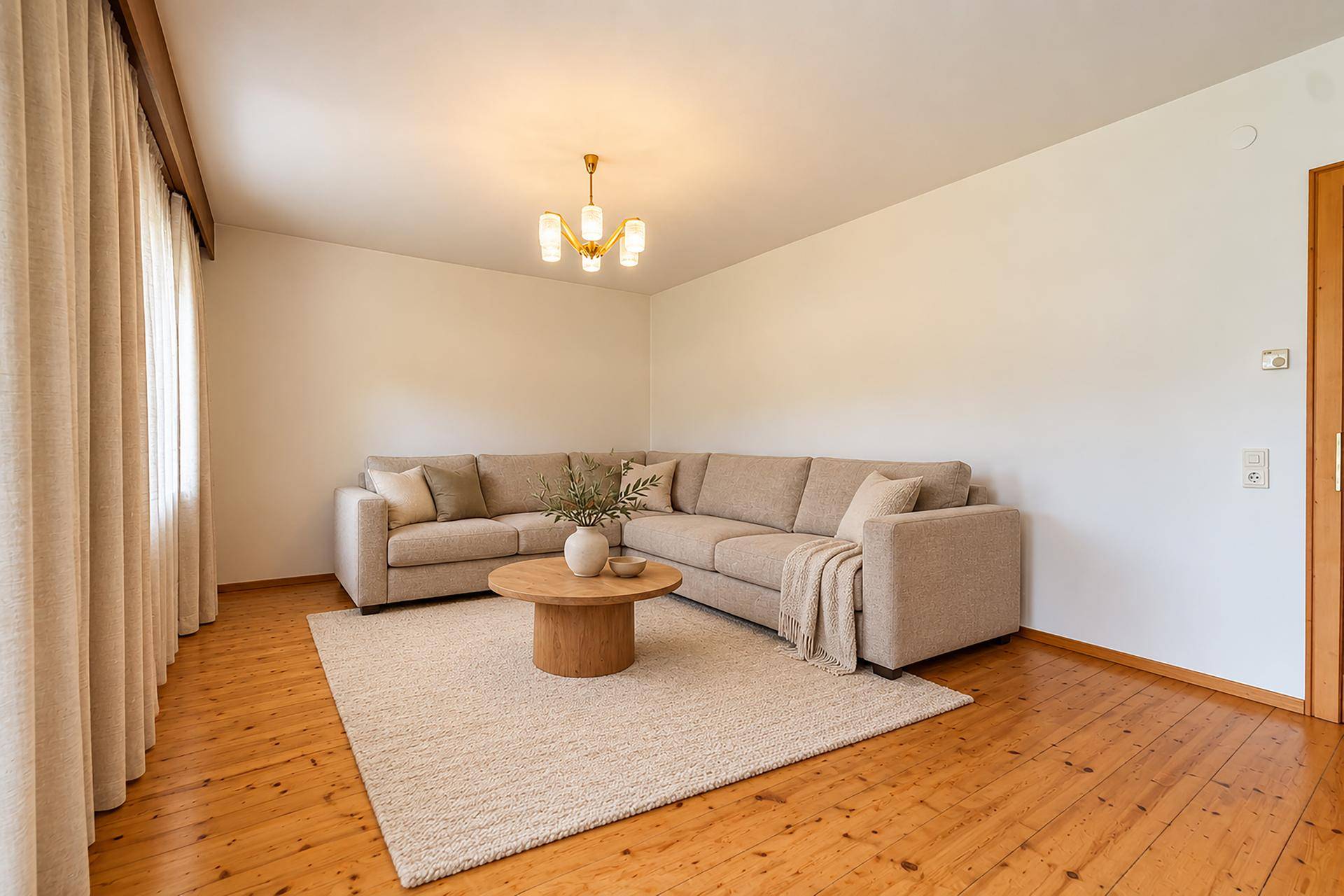 Helles Wohnzimmer mit beigem Ecksofa, Holzboden und schlichten Vorhängen, ideal zum Entspannen.