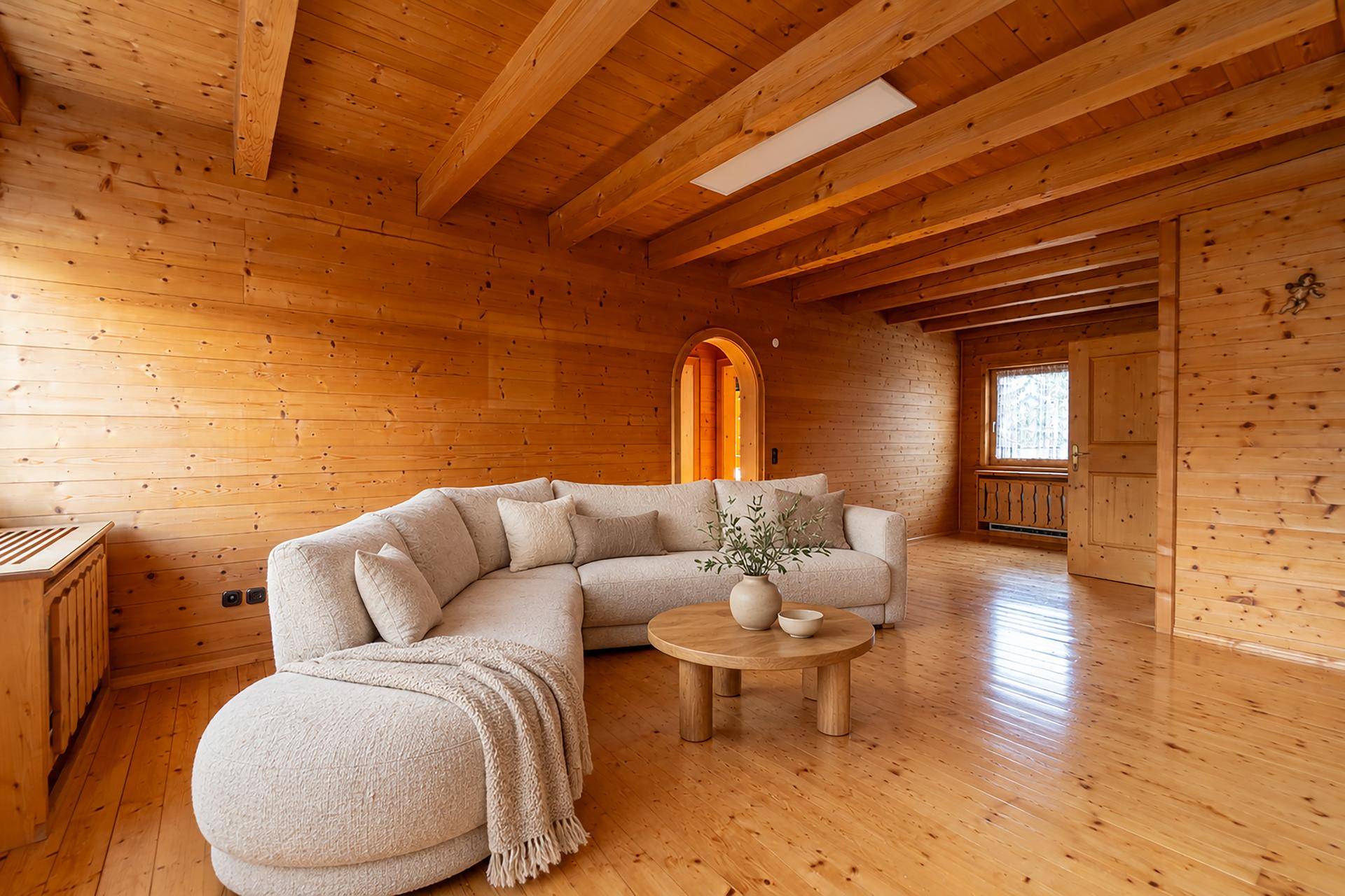 Gemütliches Wohnzimmer mit Holztäfelung an Wänden und Decke, großem Sofa und rustikalem Charme.