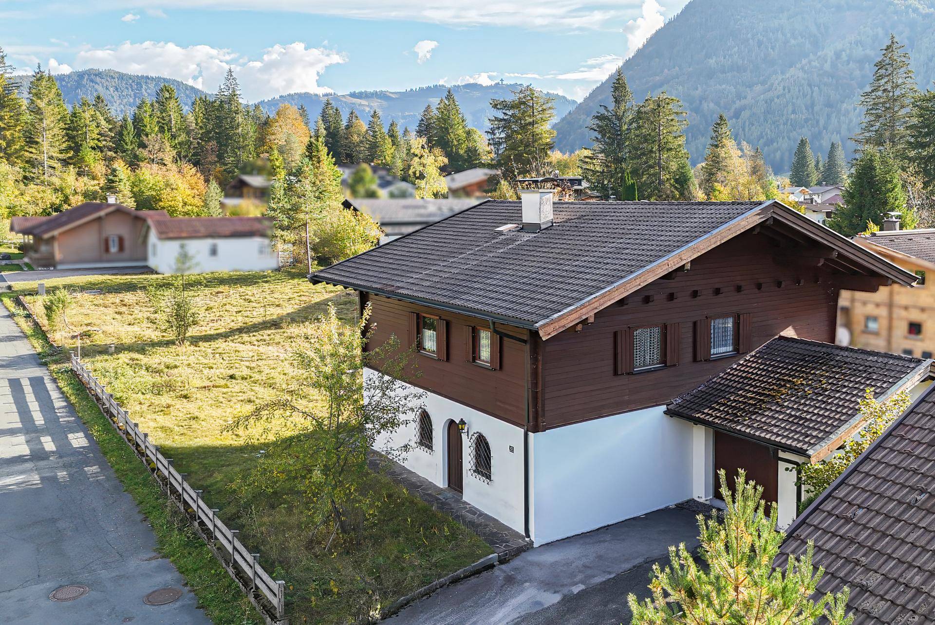 Seitenansicht des charmanten Holzhauses mit Satteldach und Zufahrt, umgeben von alpiner Natur.