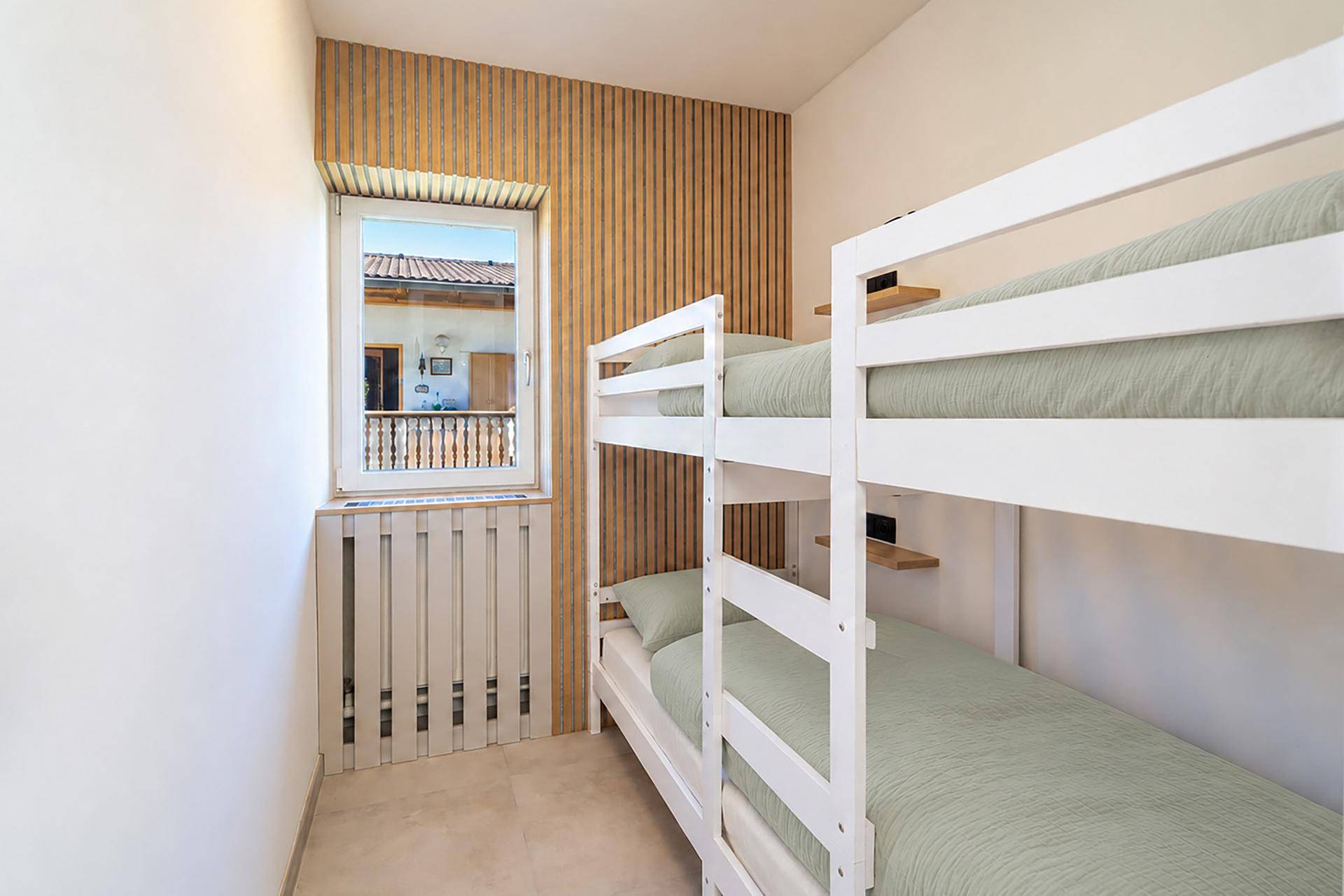 Kinderzimmer mit Etagenbetten und einem Fenster, das Tageslicht hereinlässt.