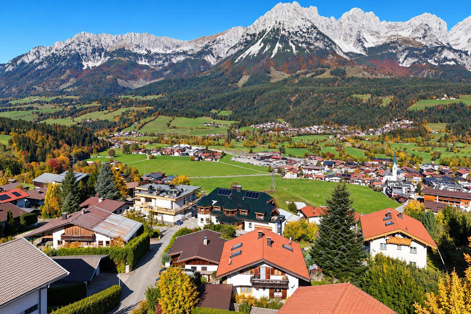 Weitläufige Ansicht eines idyllischen Dorfes, eingebettet in eine grüne Landschaft mit majestätischen Bergen.