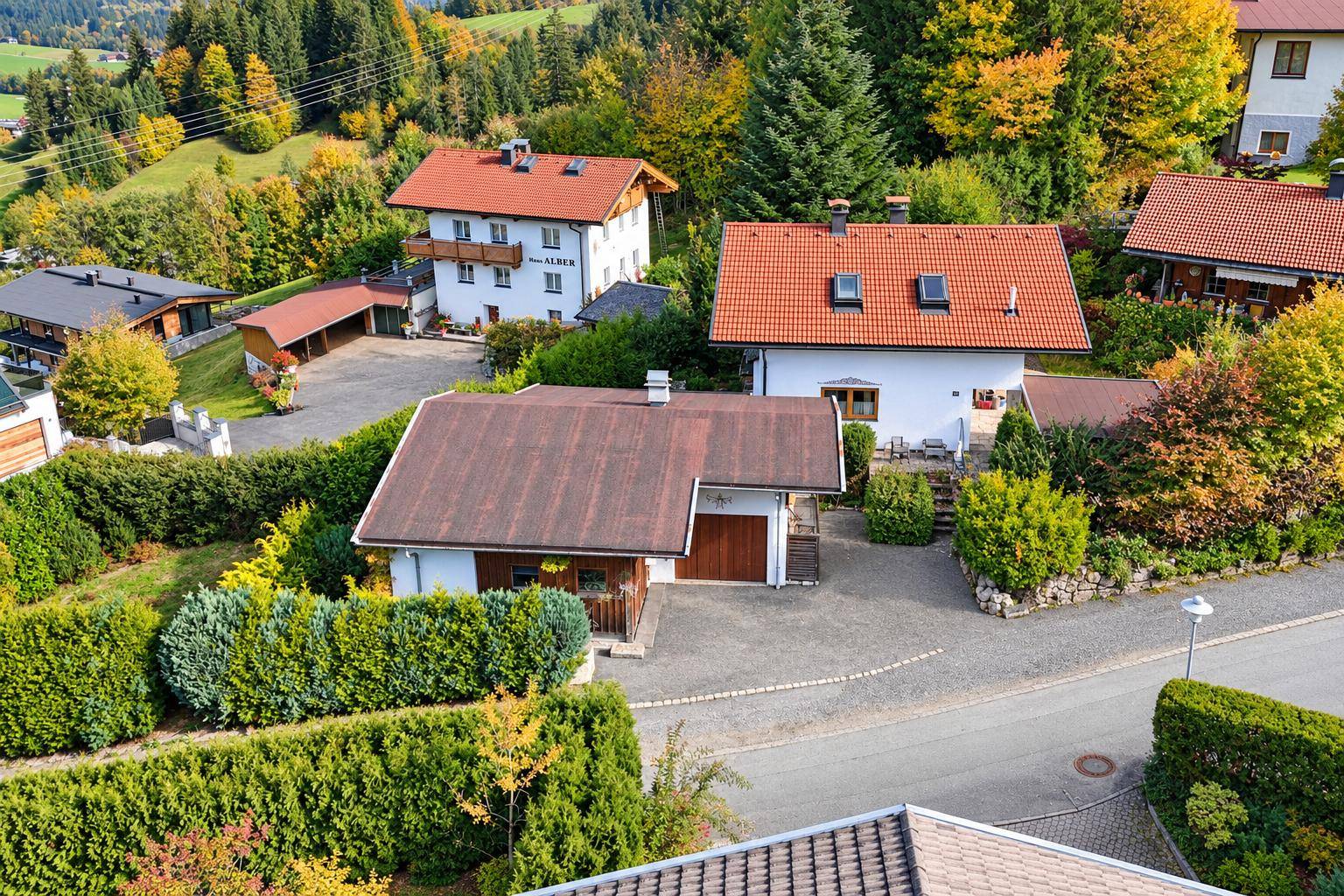 Luftaufnahme einer Wohnsiedlung mit gepflegten Gärten, Hecken und traditionellen Häusern in ländlicher Umgebung.