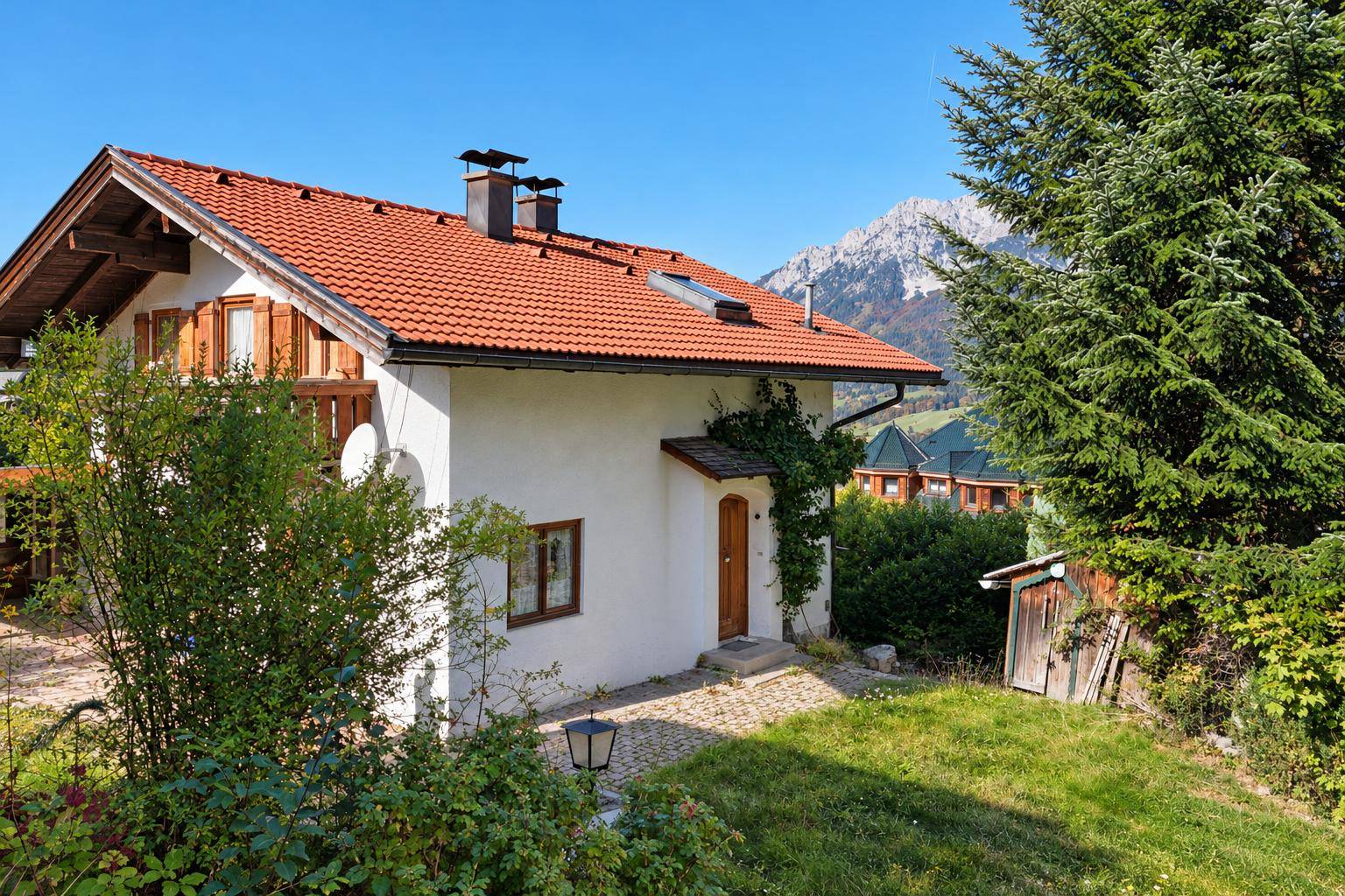 Charmantes Haus mit rotem Ziegeldach, umgeben von einem grünen Garten und einem kleinen Schuppen.