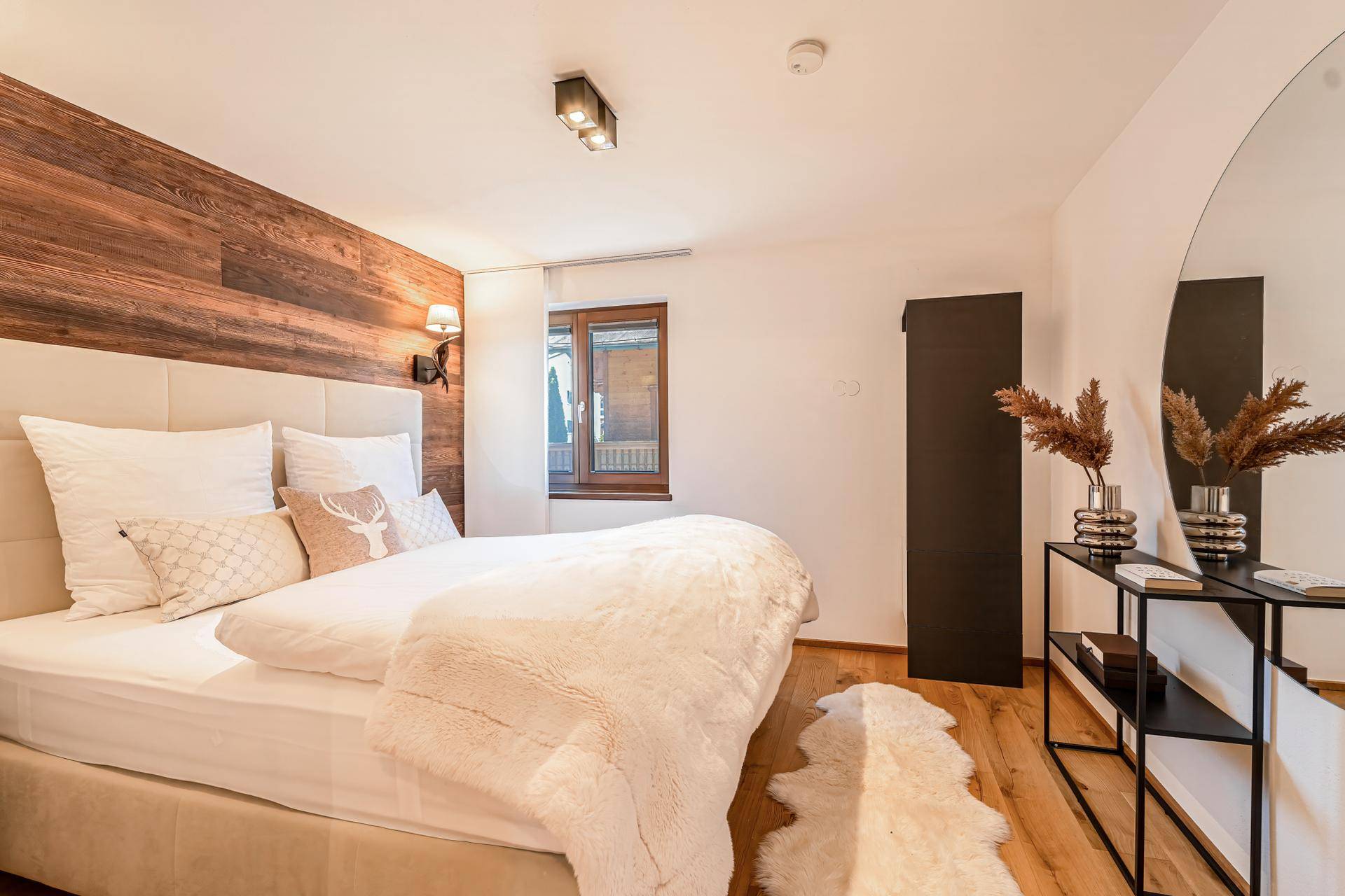 Helles Schlafzimmer mit Holzboden, großem Bett und modernem runden Spiegel als dekoratives Element.