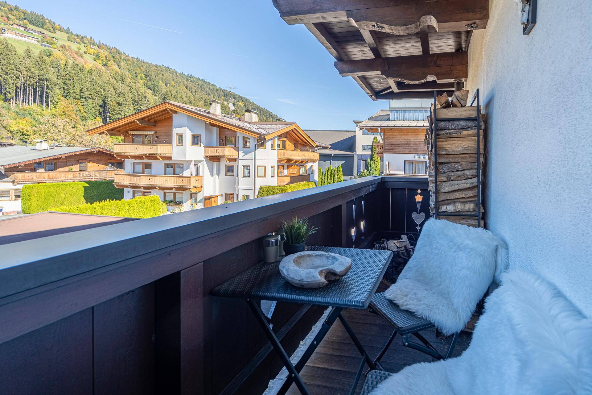 Gemütlicher Balkon mit Sitzgelegenheiten und Blick auf die umliegenden Häuser und die Bergkulisse.