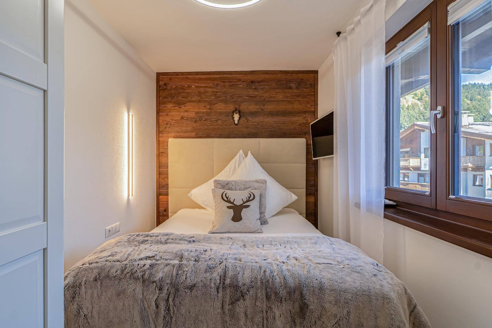 Gemütliches Schlafzimmer mit Holzwand, Doppelbett und natürlichem Lichteinfall durch das Fenster.