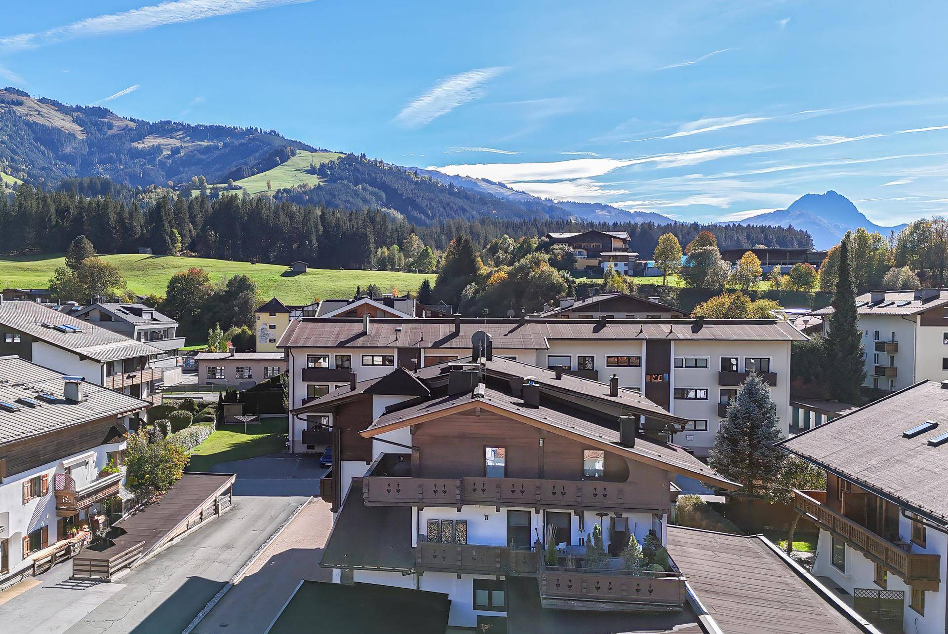 Panoramablick auf die alpine Siedlung mit traditionellen Häusern und grünen Hügeln unter blauem Himmel.