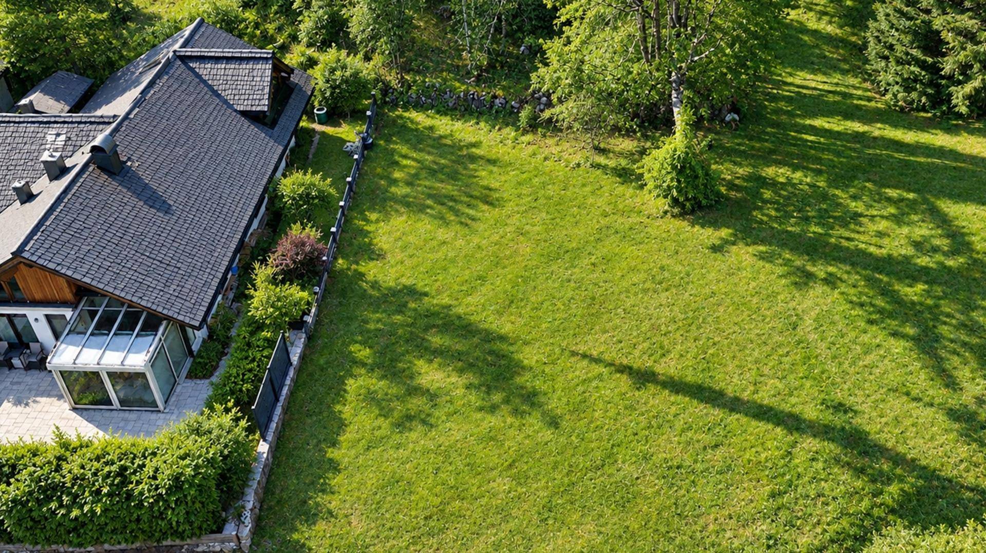 Luftaufnahme eines Hauses mit großem Garten und angrenzender Grünfläche in sonniger Lage.
