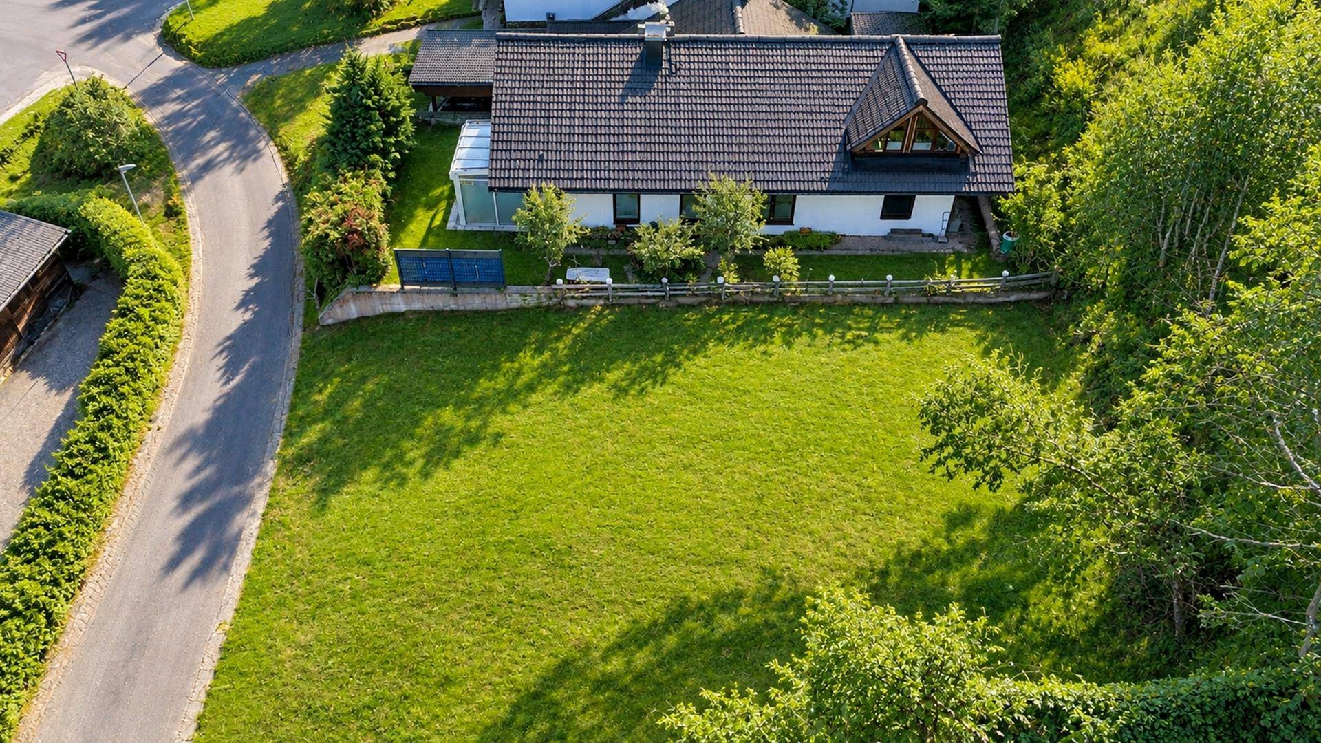 Luftaufnahme eines Einfamilienhauses mit großem Grundstück, Zufahrt und angrenzender Straße.