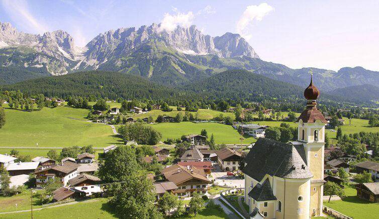 Panoramablick auf ein malerisches Alpendorf mit einer Kirche und majestätischen Bergen im Hintergrund.