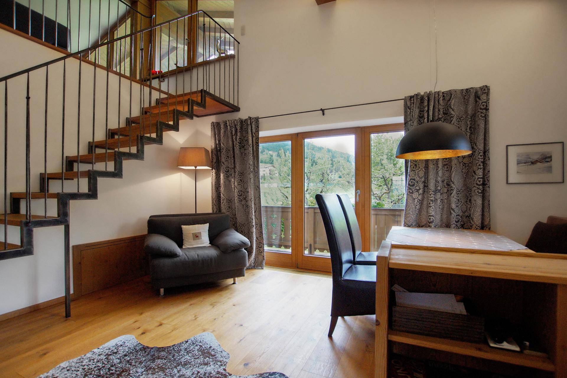 Offener Wohnbereich mit Holztreppe, die in die obere Etage führt, und Zugang zum Balkon.