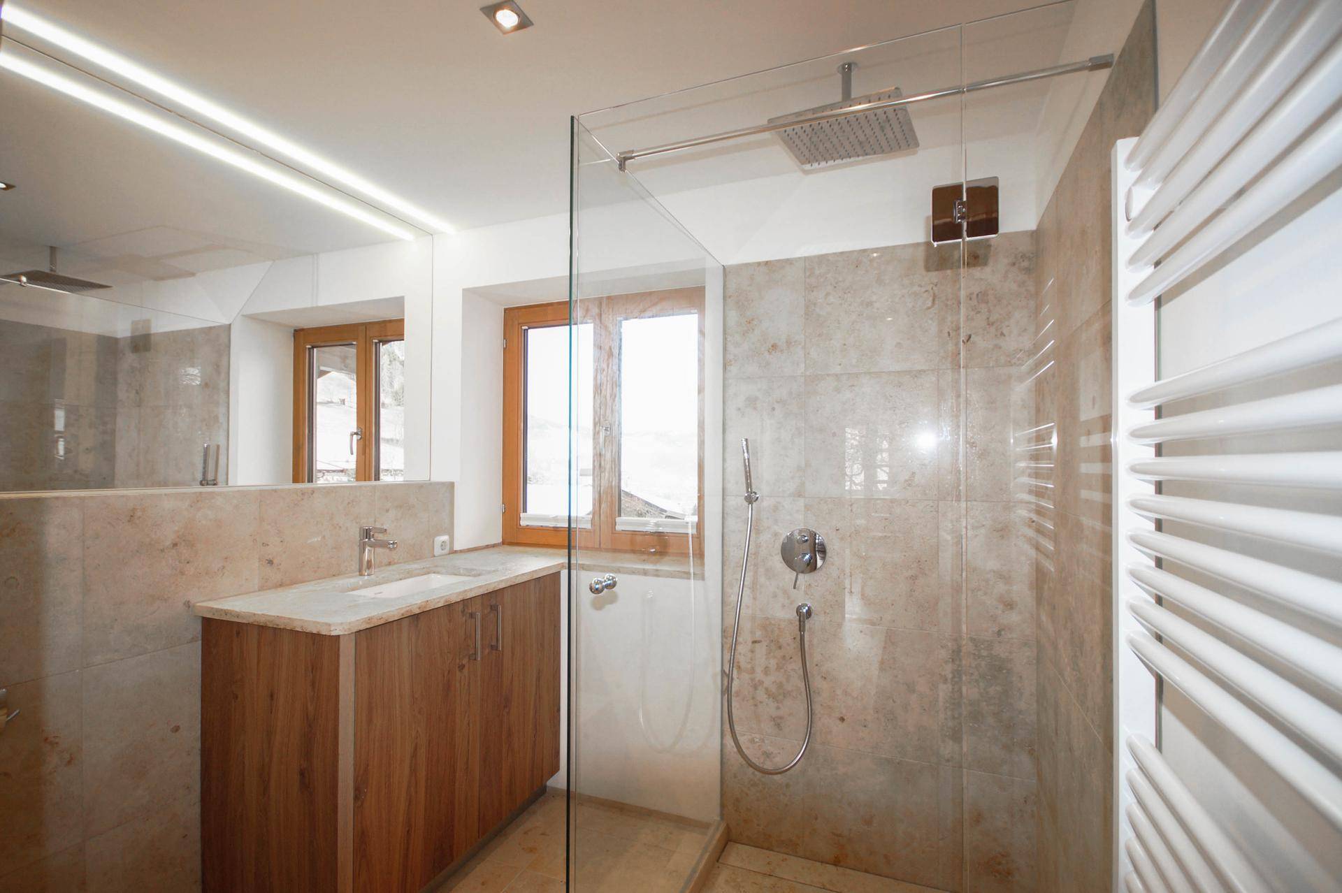 Modernes Badezimmer mit begehbarer Dusche, Natursteinfliesen und beheiztem Handtuchhalter.
