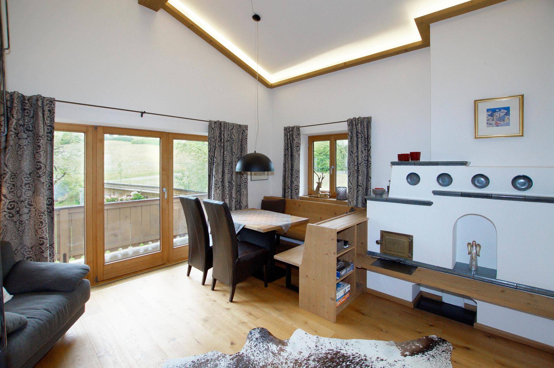 Heller Wohn- und Essbereich im alpinen Stil mit Holzboden, Kachelofen und Zugang zum Balkon.