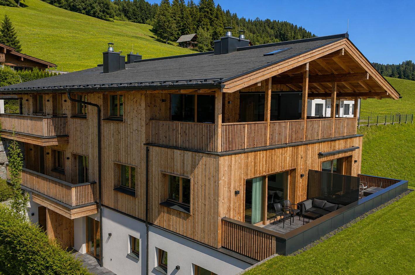 Holzverkleidetes Chalet mit mehreren Balkonen und einer möblierten Terrasse mit Bergblick.