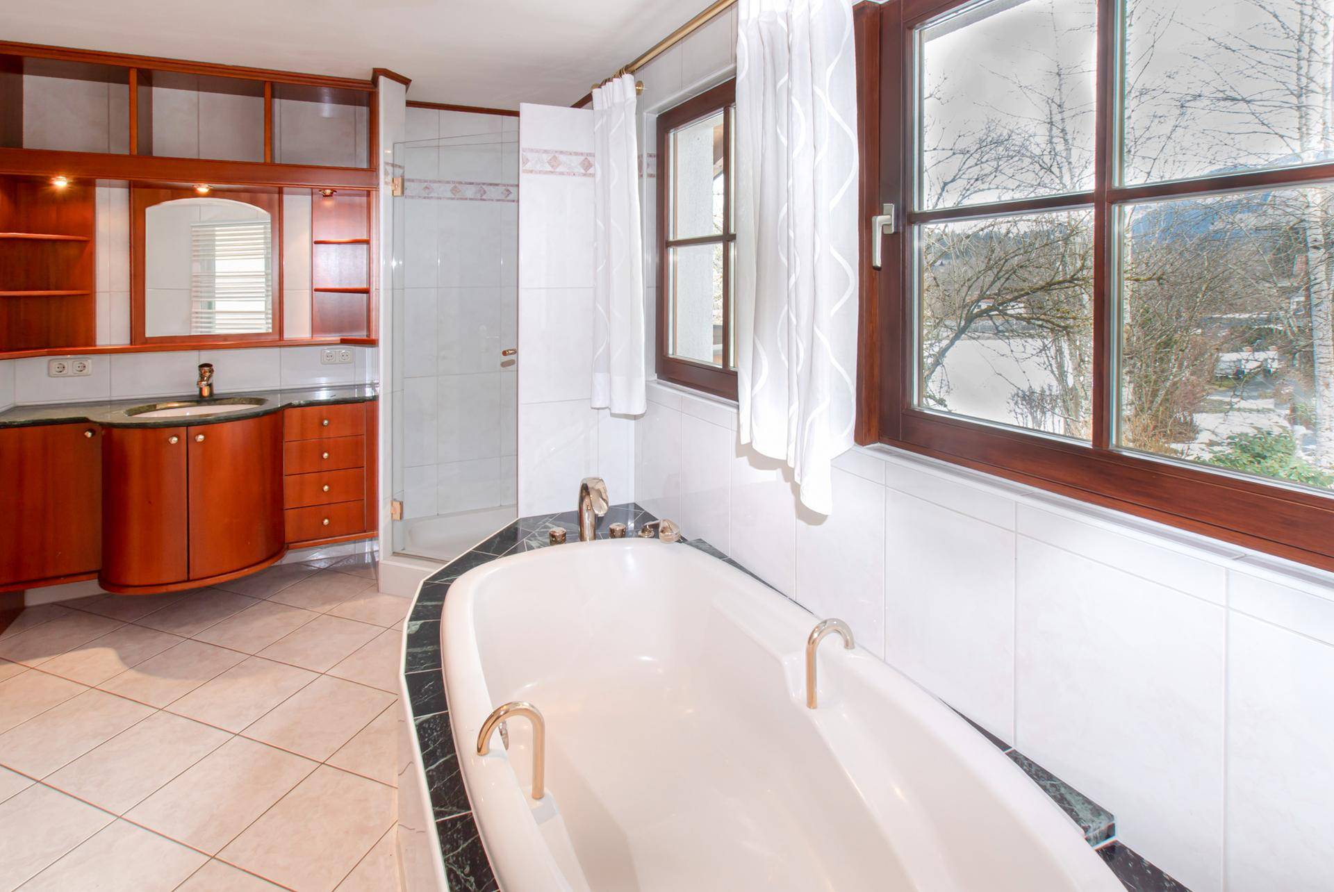 Geräumiges Badezimmer mit Badewanne, Dusche und großem Fenster mit Blick ins Grüne.