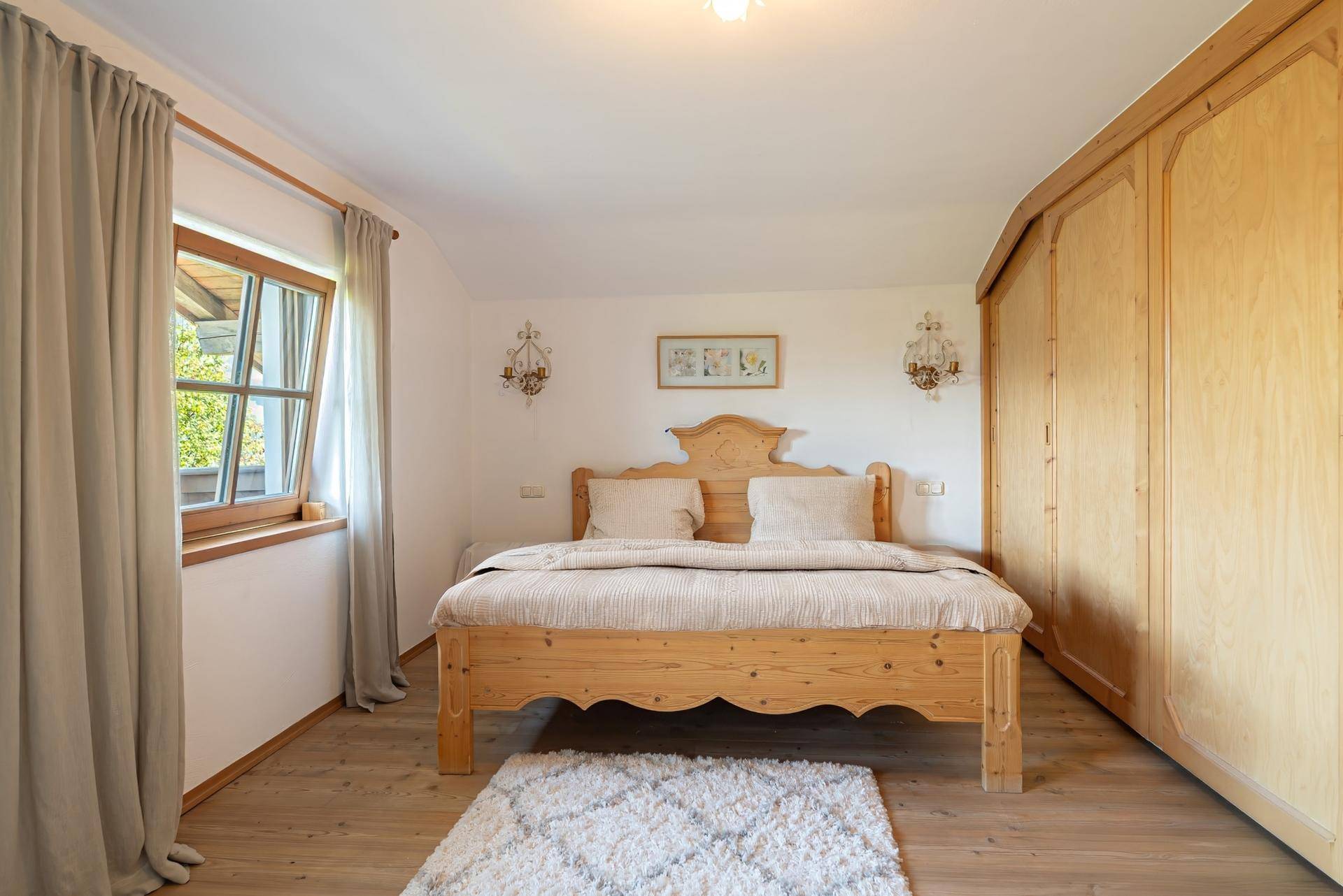 Helles Schlafzimmer mit einem Holzbett, Einbauschränken und einem Fenster mit Blick ins Grüne.