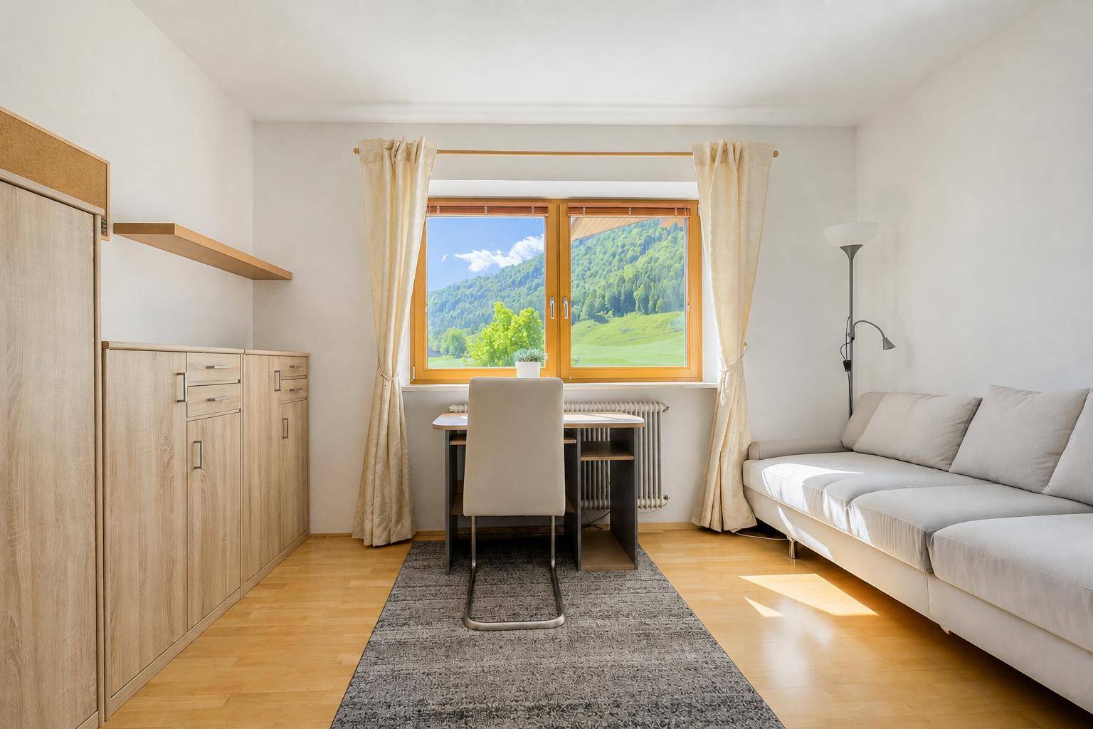 Helles Wohnzimmer mit bequemer Couch, Schreibtisch und einem schönen Bergblick durch das Fenster.