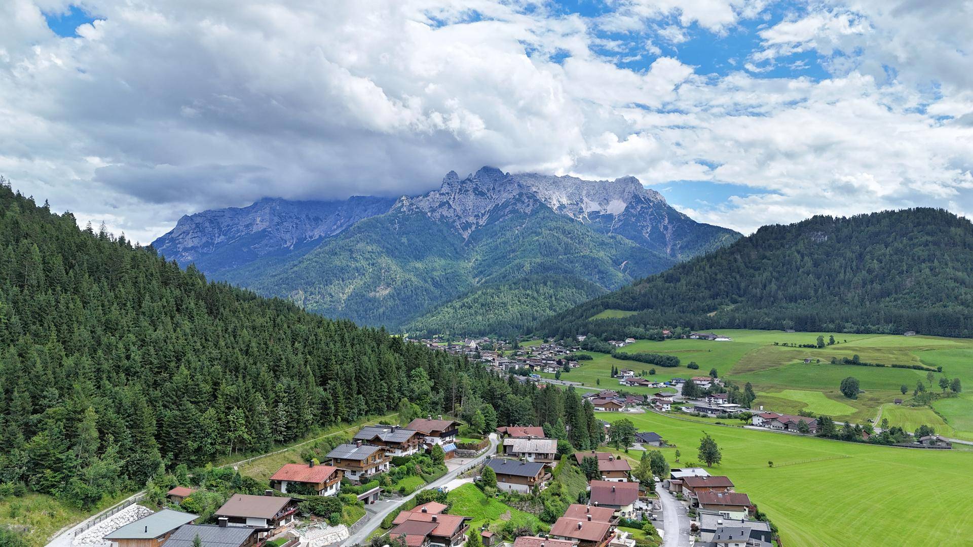 Malerische Berglandschaft mit einem Dorf im Tal unter einem bewölkten Himmel.
