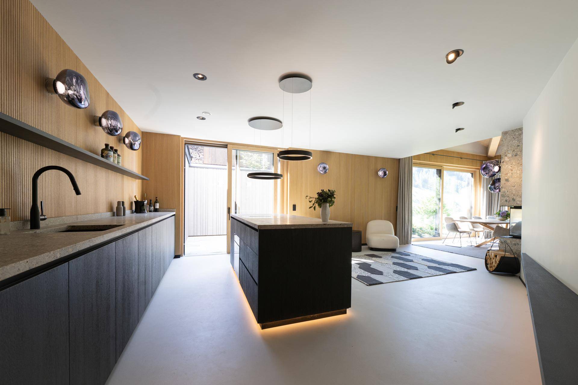Moderne Küche mit dunkler Kücheninsel, Holzvertäfelung und Zugang zum Außenbereich.