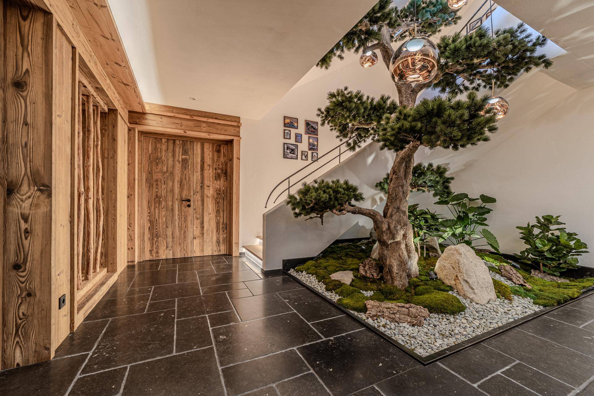 Heller Eingangsbereich mit Steinboden, Holzverkleidung und einem dekorativen Baum im Innenhof.