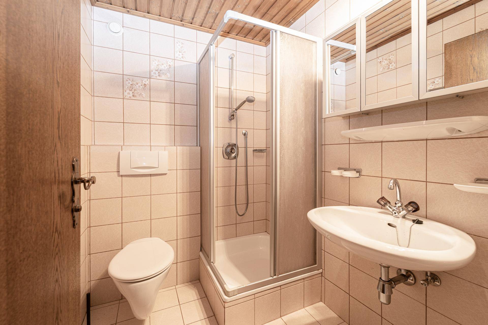 Helles Badezimmer mit Duschkabine, WC, Waschbecken und hellen Fliesen.