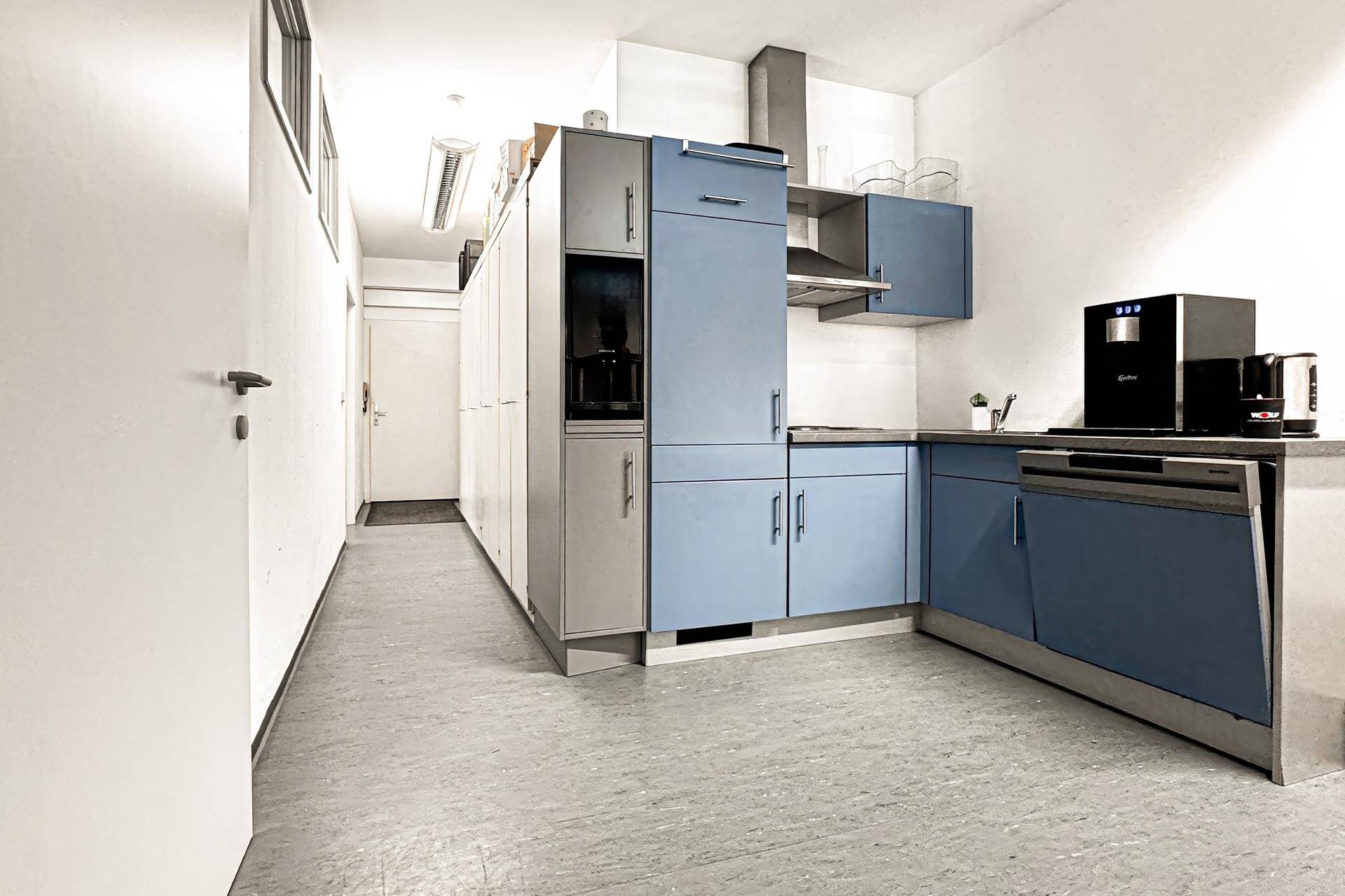Moderne Teeküche mit blauen und grauen Schränken, Spülmaschine und Kaffeemaschine.