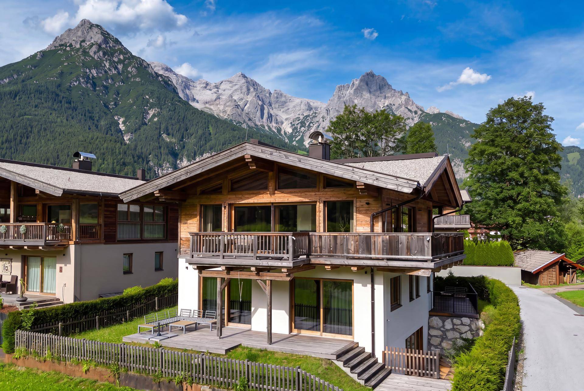 Exklusives Holzchalet mit weitläufiger Terrasse und Balkon, eingebettet in eine grüne Alpenlandschaft.
