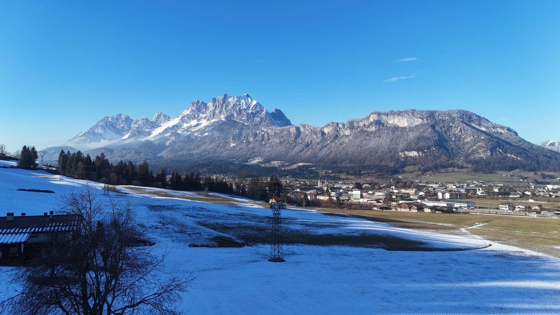 Weitläufige Winterlandschaft mit schneebedeckten Bergen und einem Dorf im Tal.
