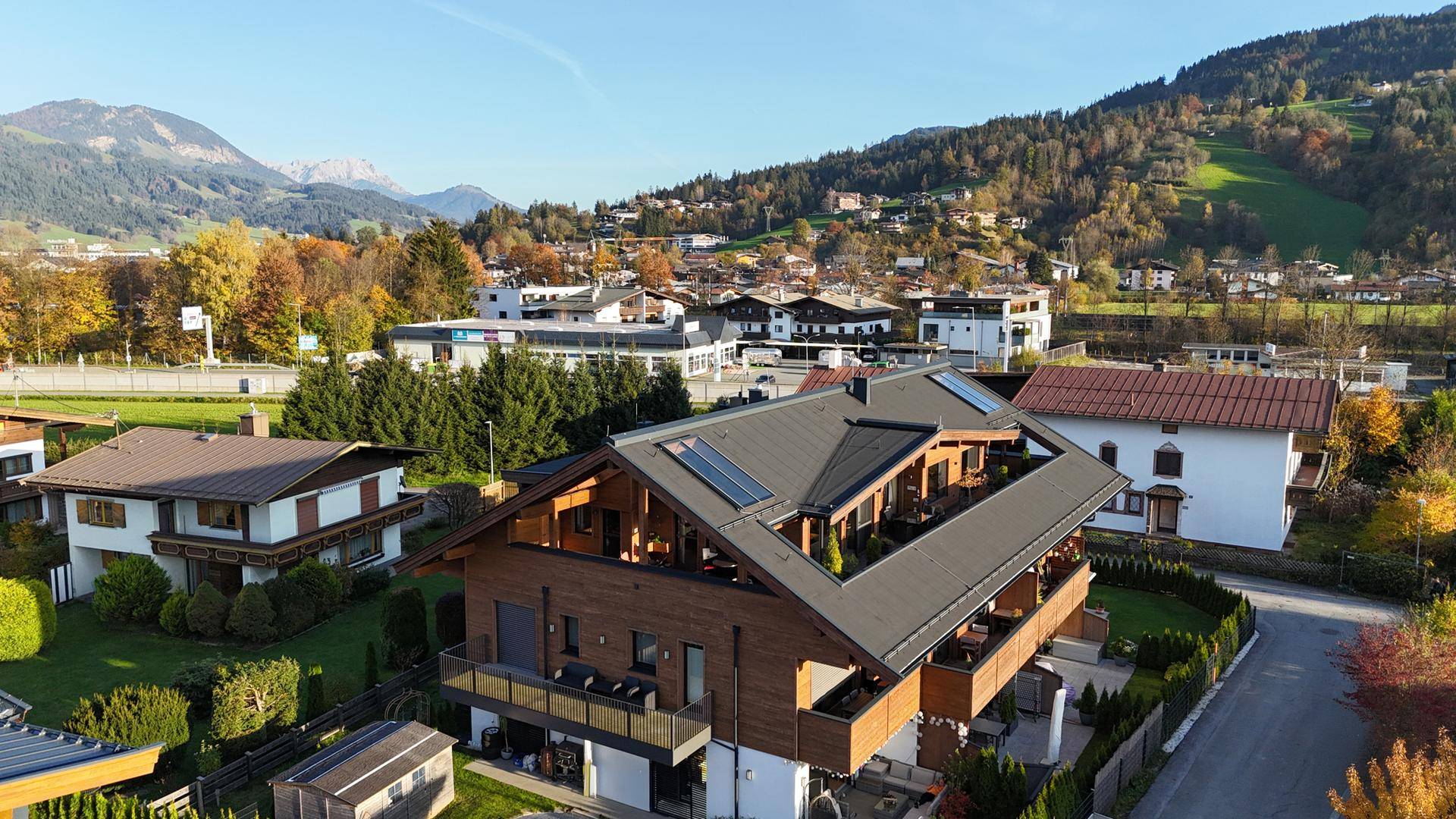 Weitläufige Luftaufnahme des modernen Chalets mit umliegender Bebauung und grüner Hügellandschaft.