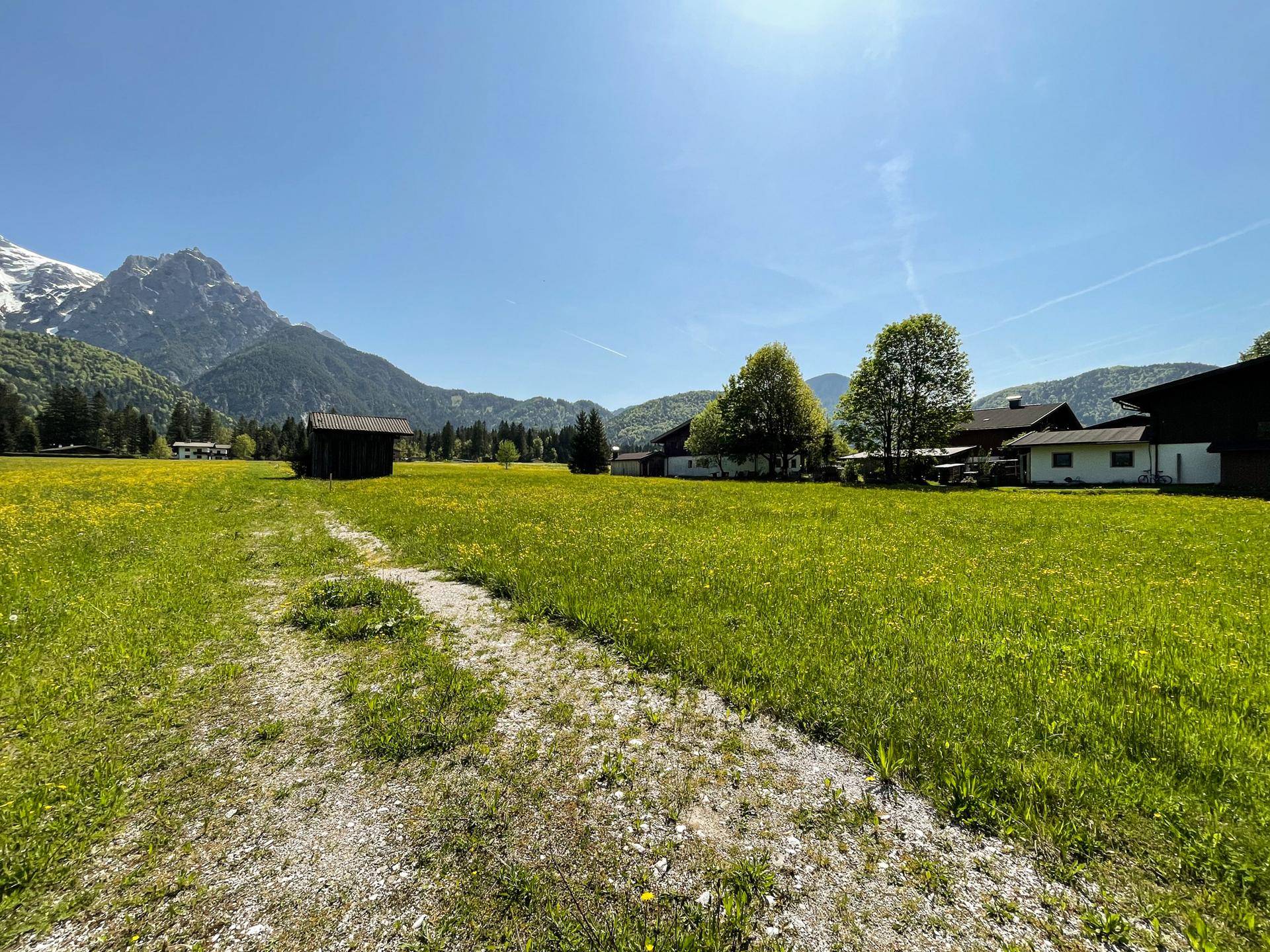 Weite Wiesenlandschaft mit Blick auf schneebedeckte Berge und ländliche Bebauung.