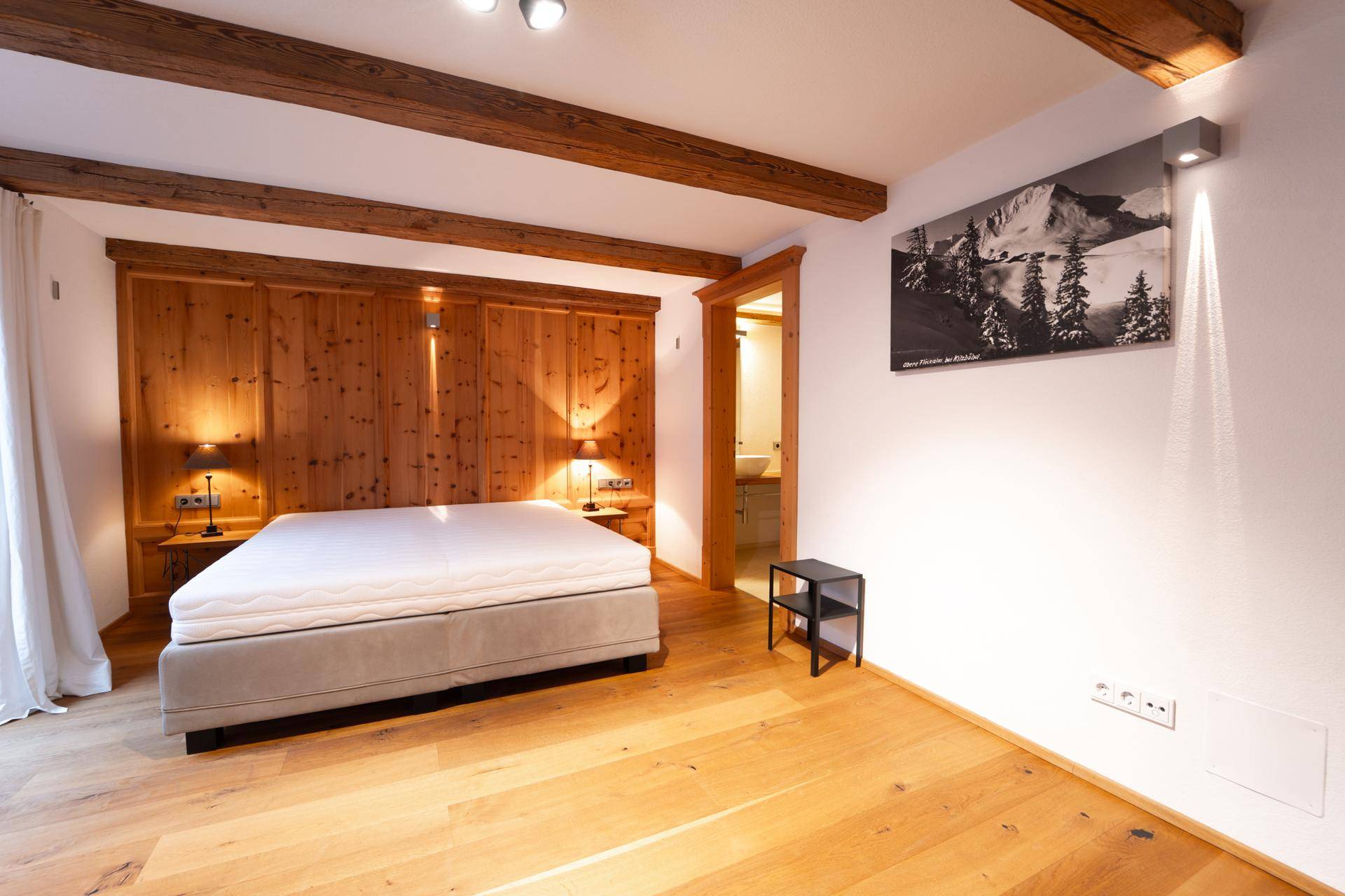 Gemütliches Schlafzimmer mit Holzwand, Holzbalken und Zugang zum Badezimmer.