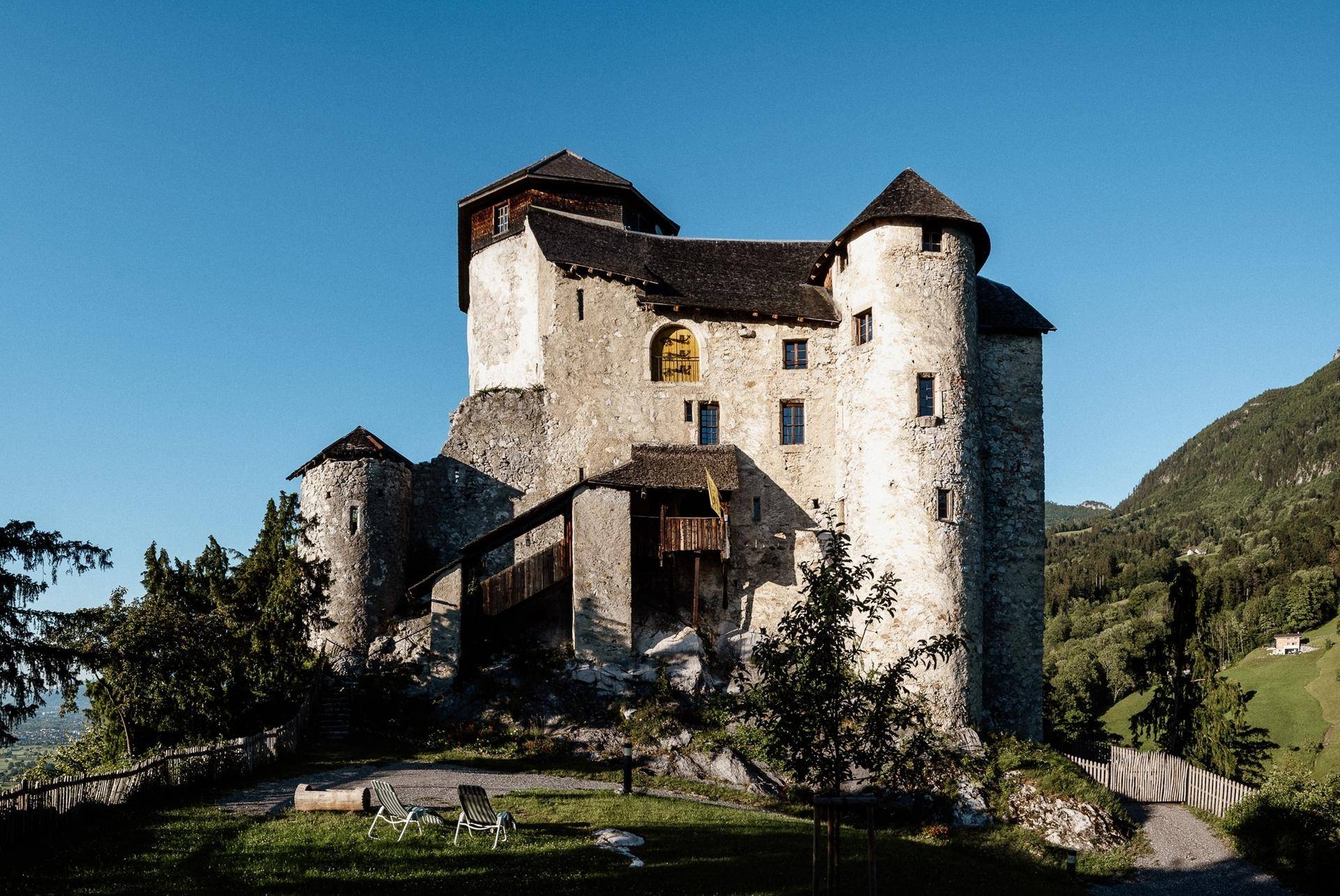 Historisches Schloss mit Steinfassade und einem kleinen Rasenbereich mit Liegestühlen.