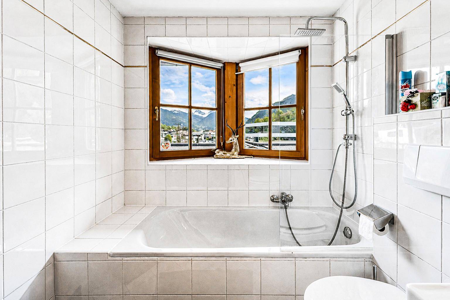 Gefliestes Badezimmer mit Badewanne, Dusche und Fenster mit Bergblick.