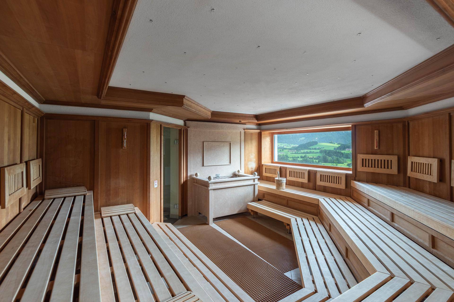 Geräumige Holzsauna mit mehreren Bänken und einem Fenster, das einen Blick ins Grüne bietet.