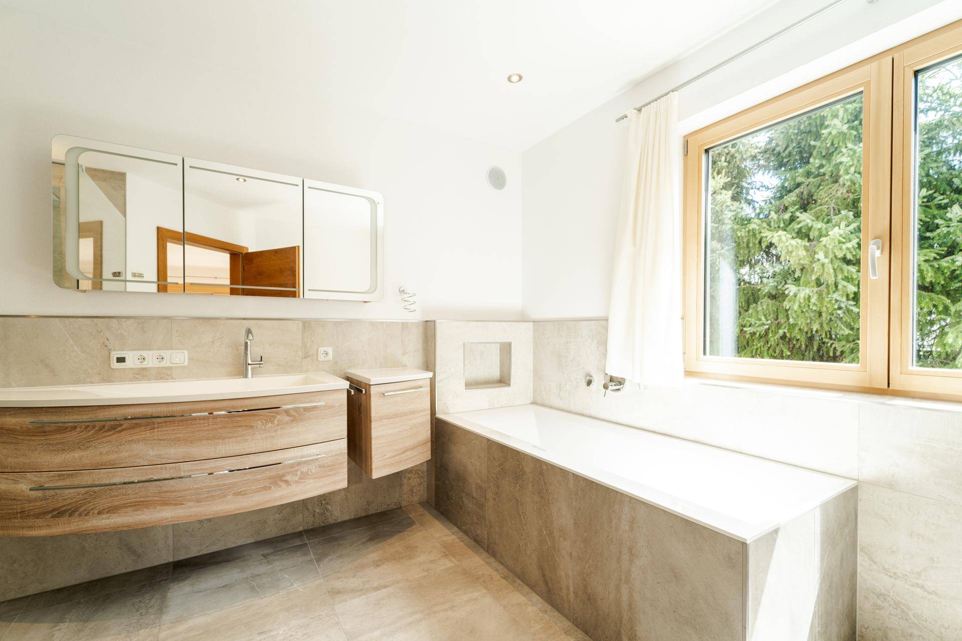 Modernes Badezimmer mit Badewanne, elegantem Waschtisch und Fenster für Tageslicht.