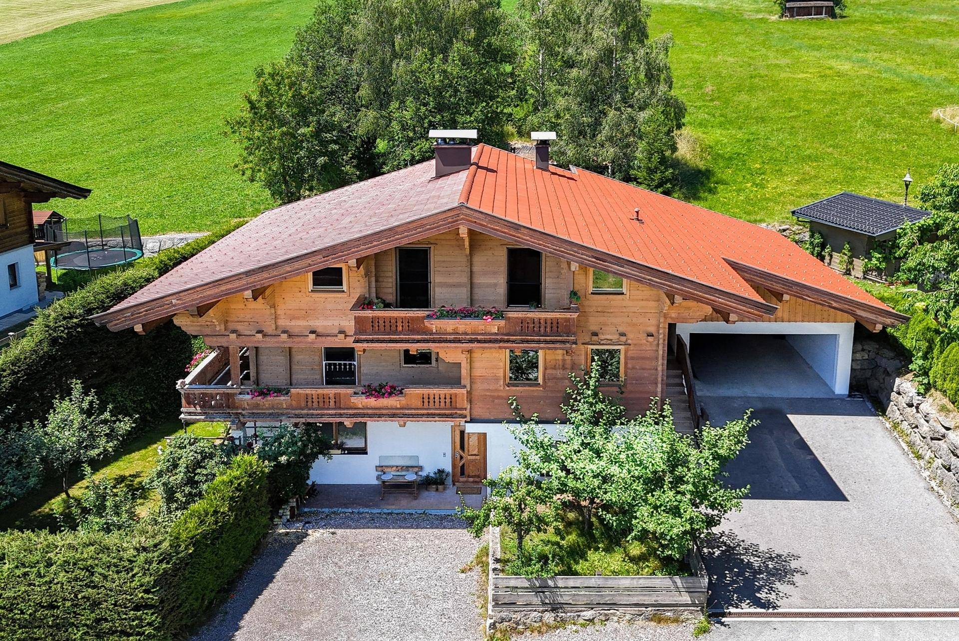 Traditionelles Holzhaus mit rotem Dach, Balkonen und integrierter Garage in ländlicher Umgebung.