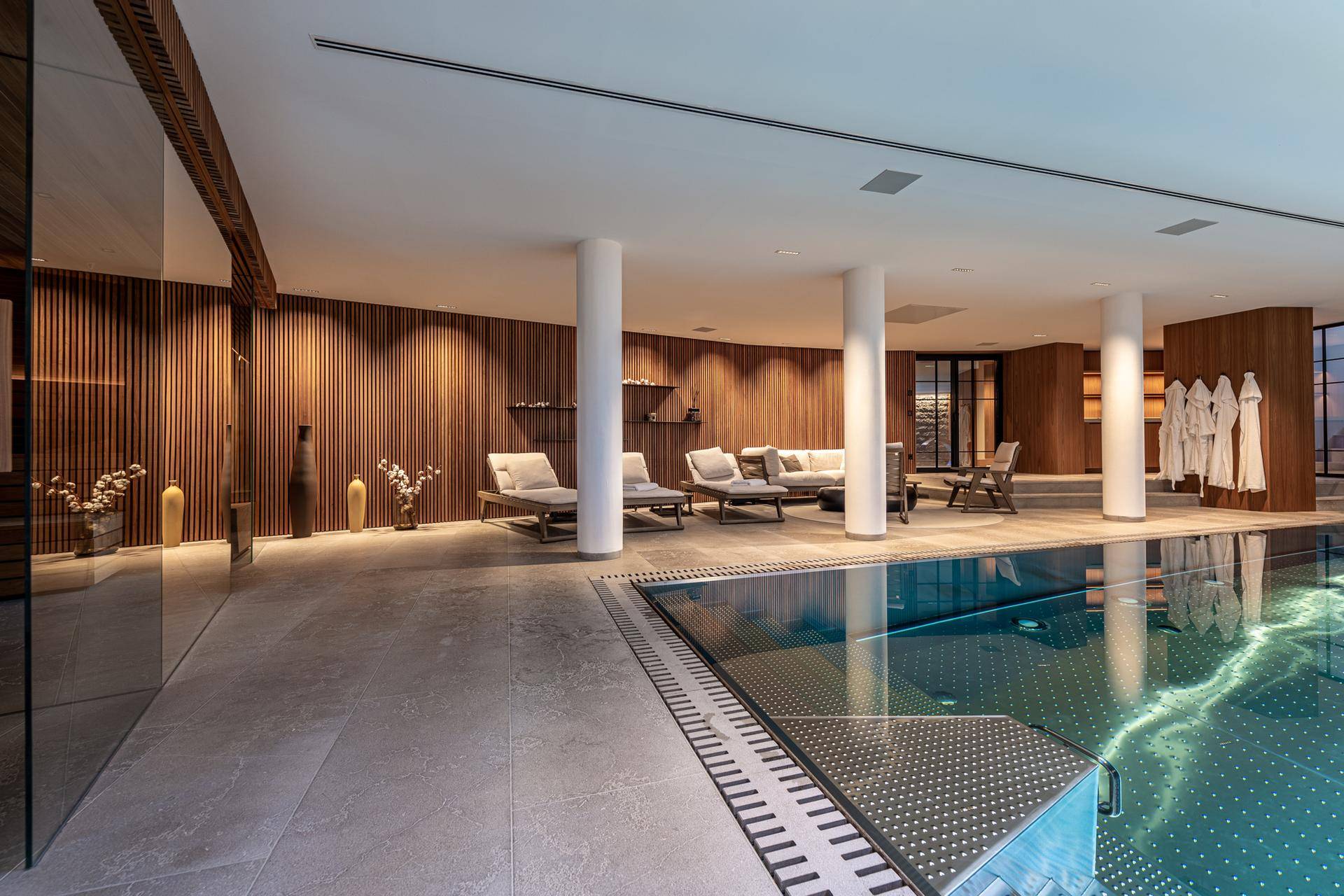 Luxuriöser Innenpoolbereich mit Liegestühlen, Holzwänden und Säulen.