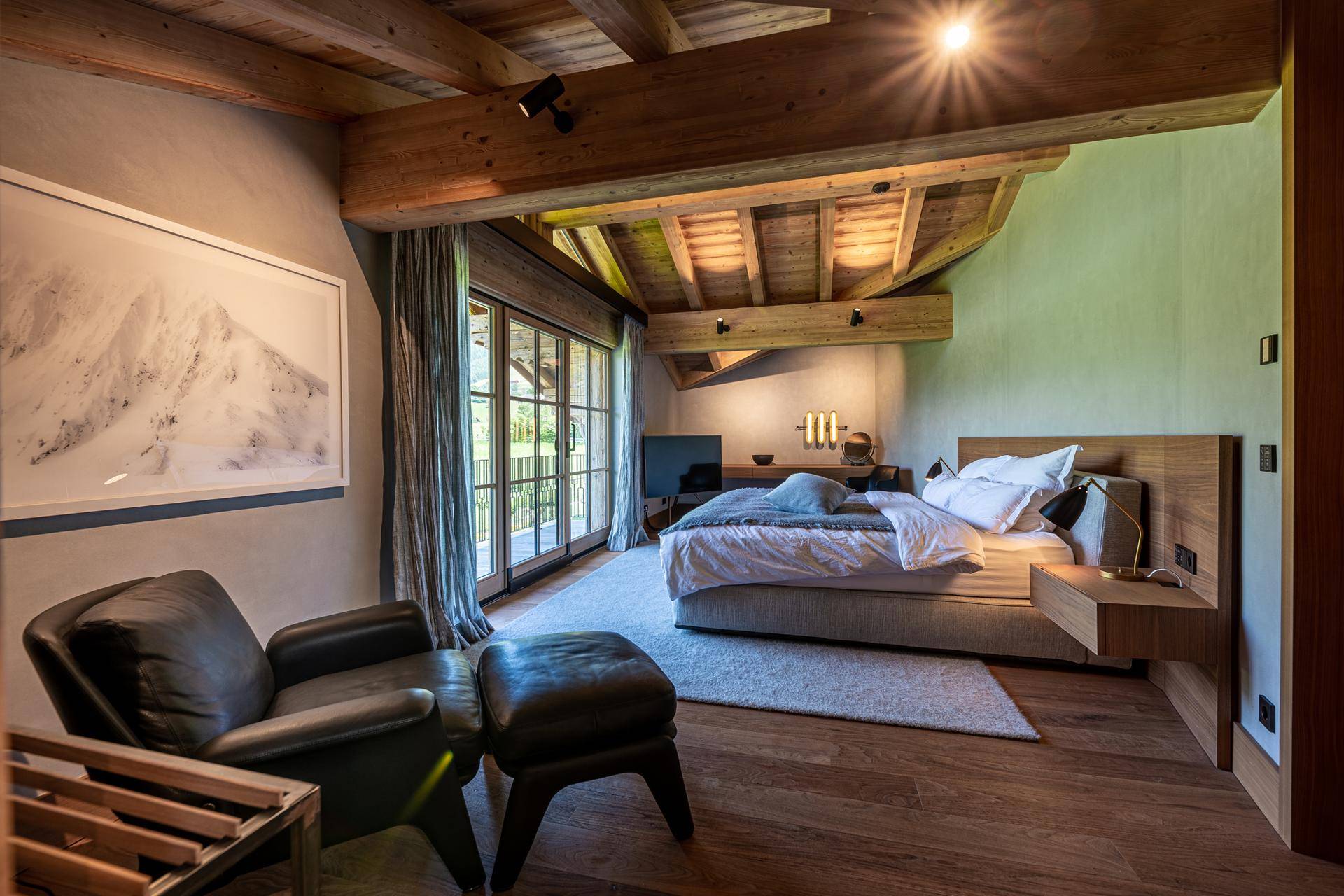 Geräumiges Schlafzimmer mit Holzbalkendecke, großem Fenster und Blick auf die Natur.