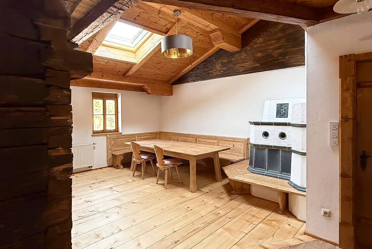 Gemütlicher Essbereich mit traditionellem Kachelofen, Holzboden und Holzbänken unter einem Dachfenster.
