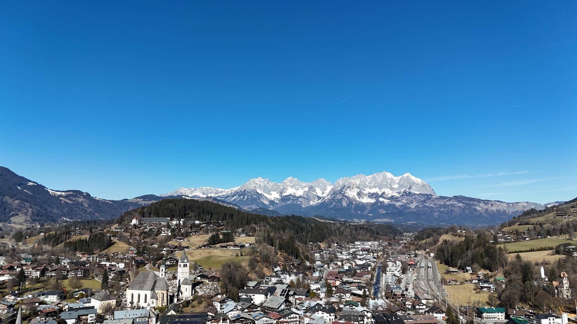 Weitläufige Luftaufnahme einer Stadt im Tal mit schneebedeckten Bergen im Hintergrund.