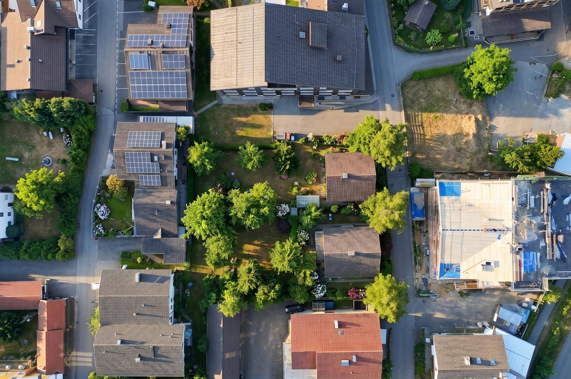 Senkrechte Luftaufnahme einer Wohnsiedlung mit Häusern, Gärten, Straßen und Solaranlagen auf Dächern.