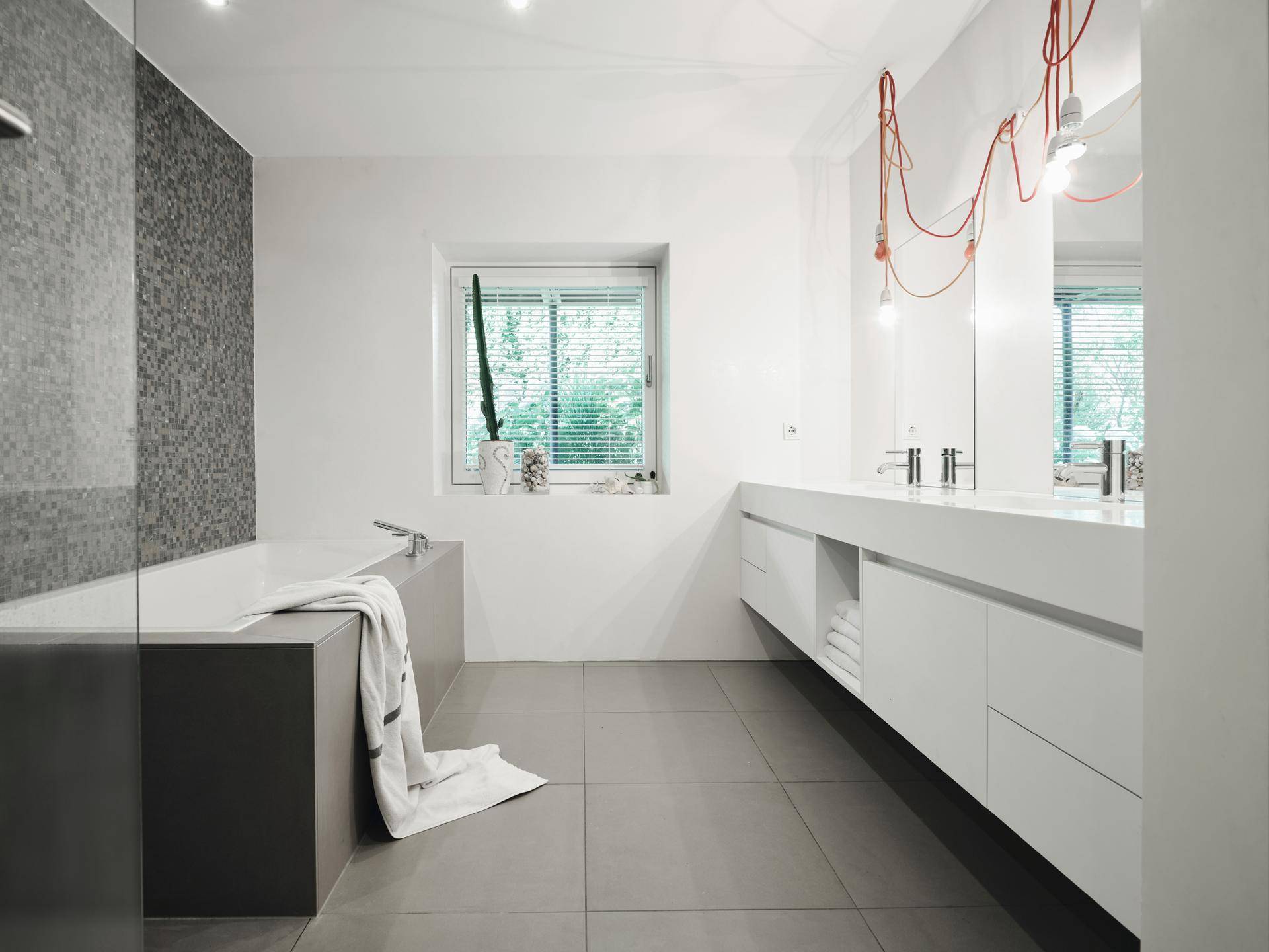 Helles, modernes Badezimmer mit Doppelwaschbecken, Badewanne und großen Fliesen.