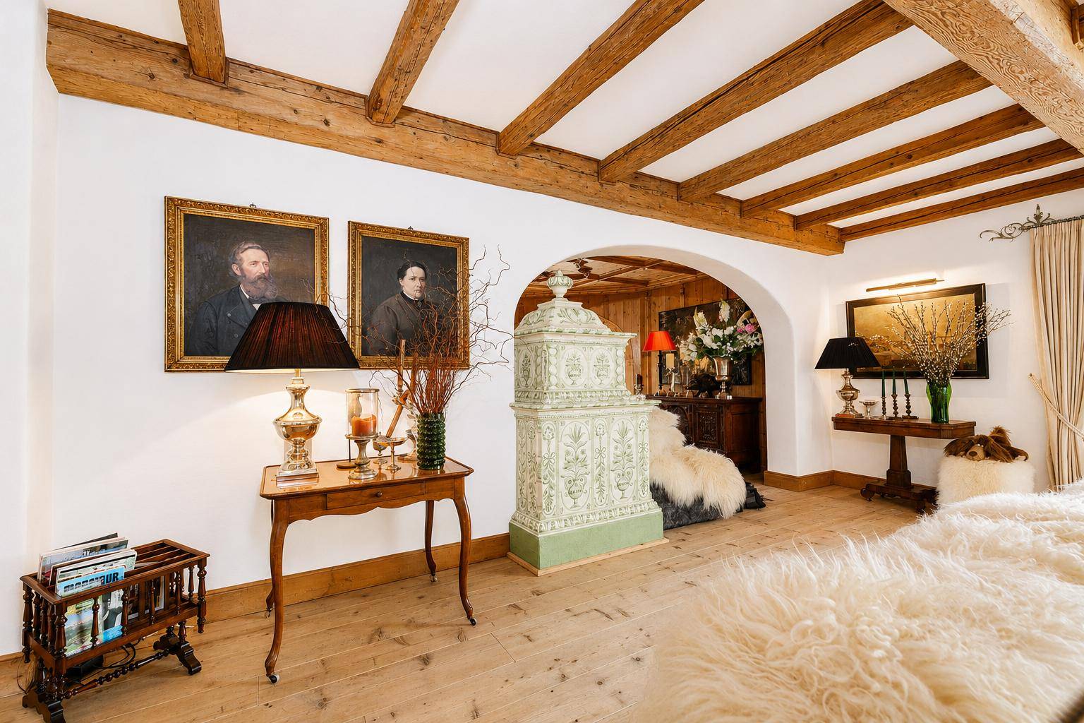 Heller Wohnbereich mit traditionellem Kachelofen, Holzbalkendecke und rustikalen Details.