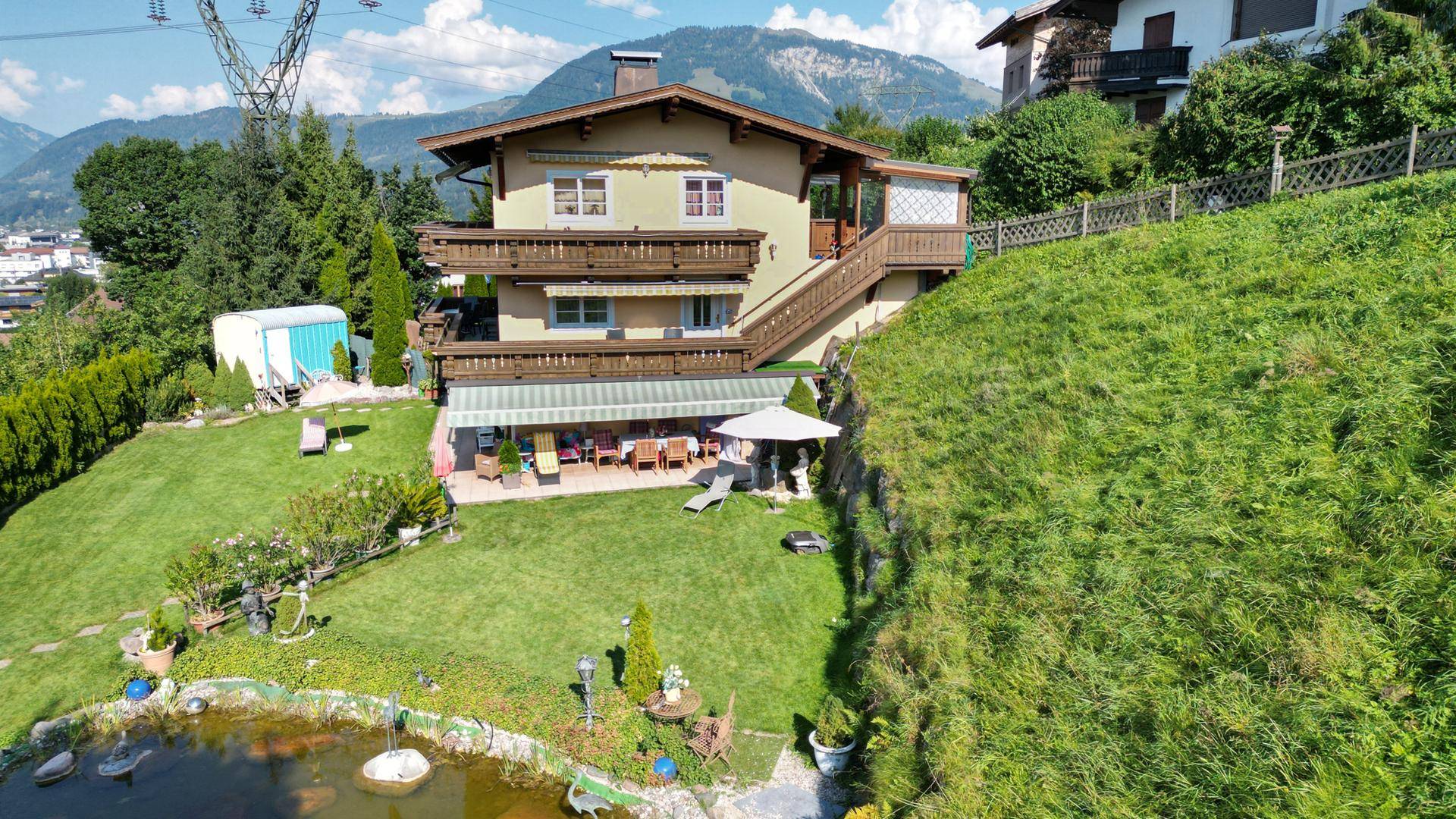 Nahaufnahme des Hauses mit großem Garten, Teich und überdachter Terrasse mit Bergblick.